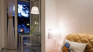 A room with a bed, a table with a lamp, a chair, and a window with curtains. - Hotel Eros Residence (Cervia)