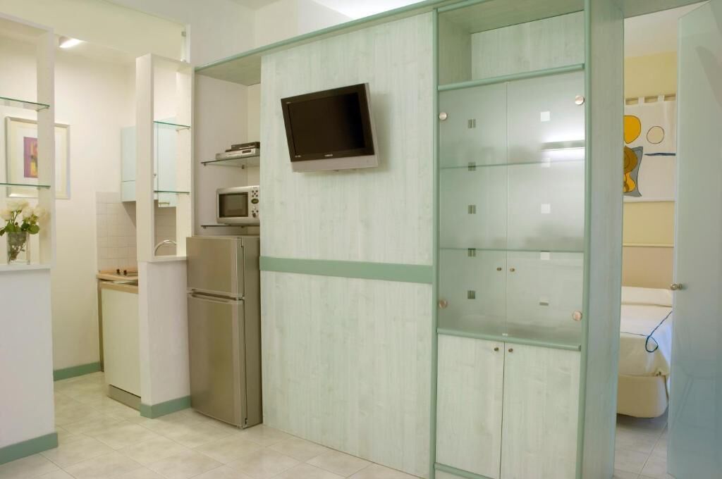 Una cocina moderna con microondas integrado, un refrigerador de acero inoxidable y un armario de vidrio con un televisor de pantalla plana montado encima.