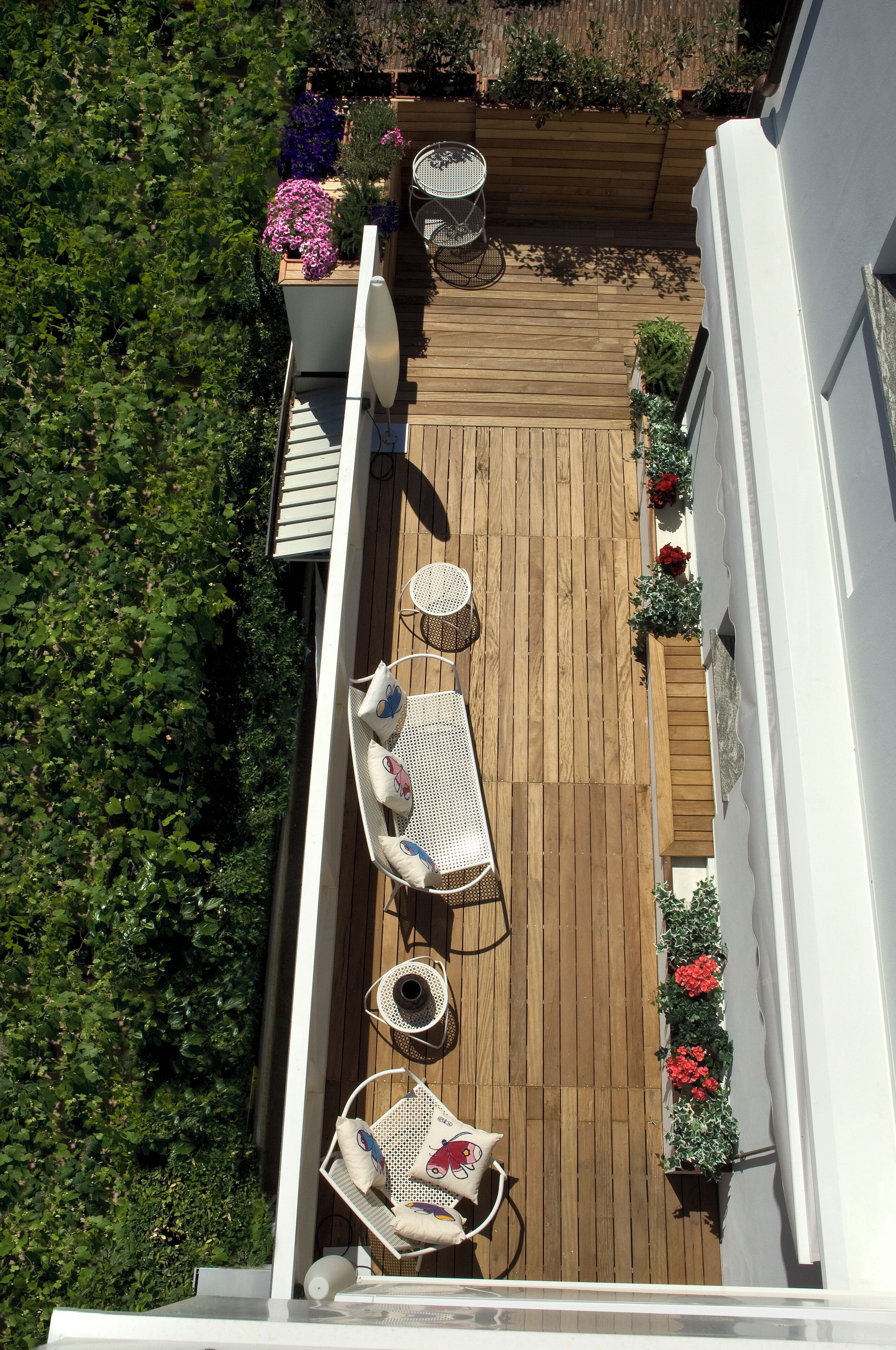 Una terraza en la azotea con suelo de madera, mobiliario exterior blanco y plantas en macetas.