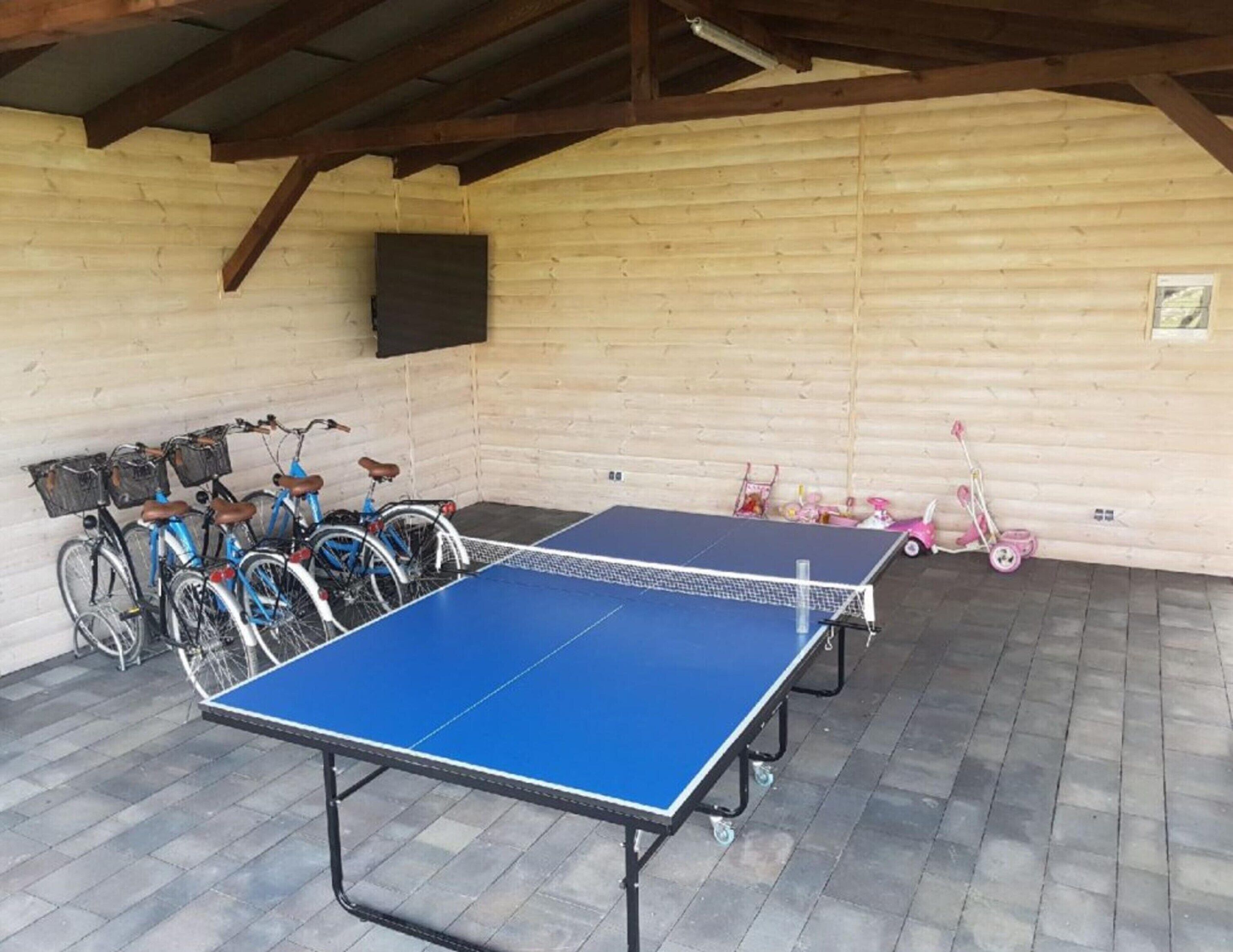 Una mesa de ping pong en un espacio cubierto, con bicicletas y juguetes infantiles.