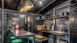Une cuisine compacte avec un coin bar, des tabourets verts et une poubelle.