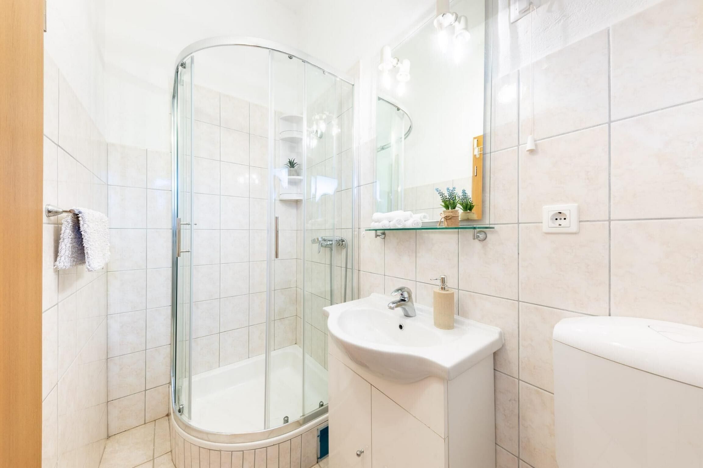 Un baño moderno con ducha envuelta en vidrio, un lavamanos blanco y un inodoro.