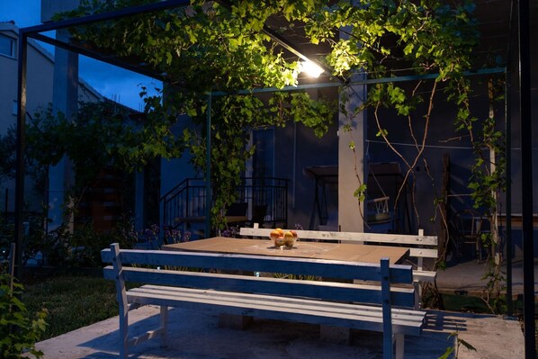 A wooden bench with a bowl of fruit in the center, under a pergola with climbing plants.