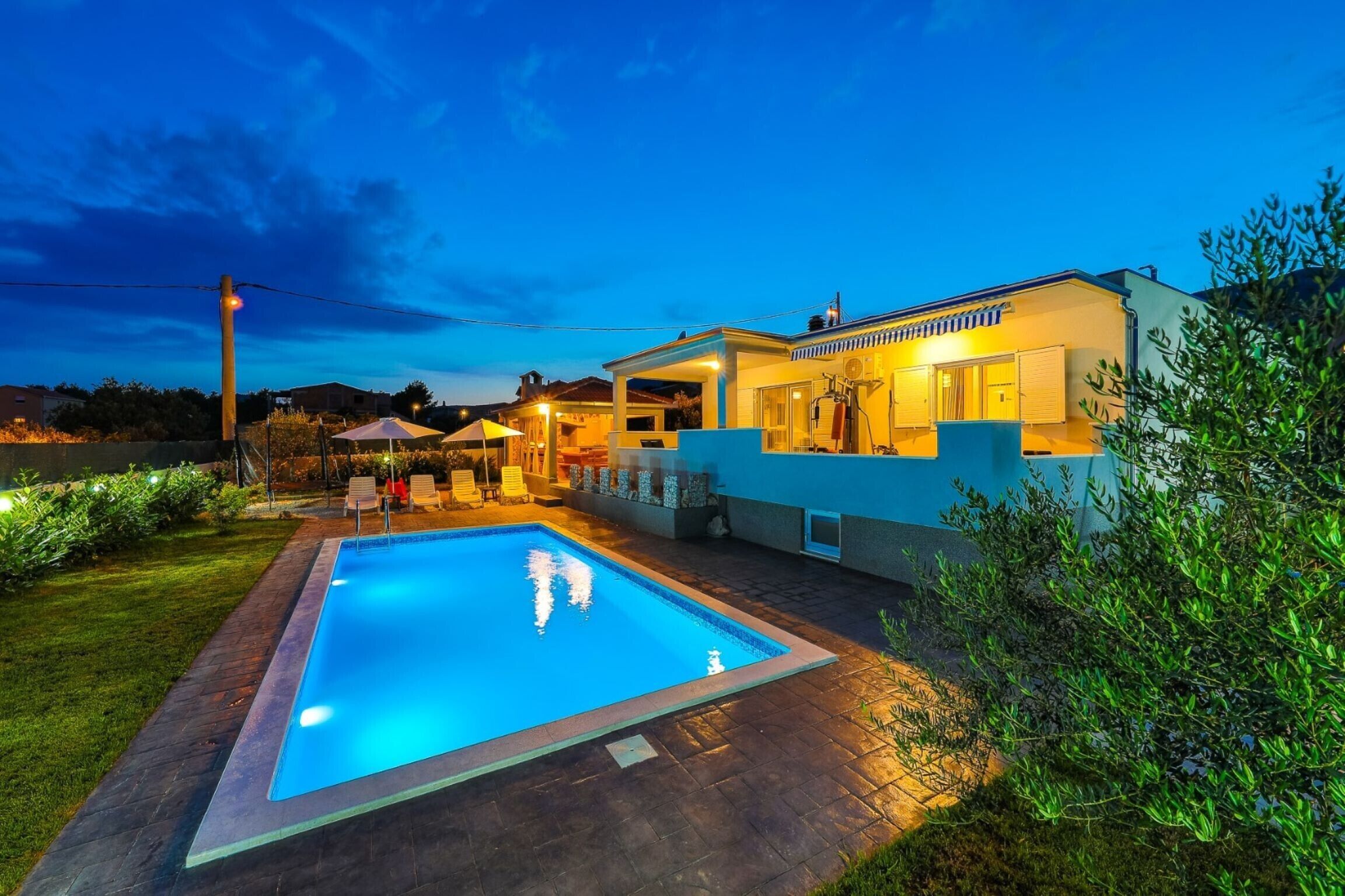 Ein modernes Haus mit Swimmingpool, Sitzgelegenheiten im Freien und einer gut beleuchteten Terrassenfläche.