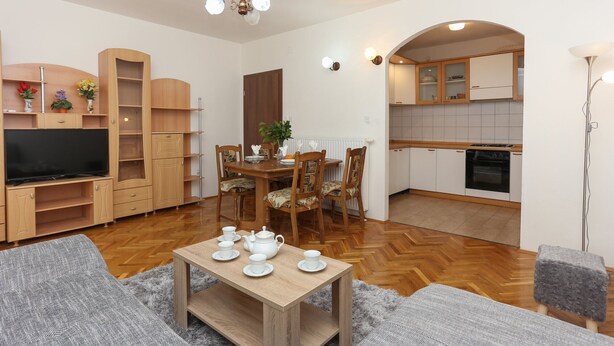 Ein modernes Wohnzimmer mit einem Holzesstisch, gedeckt für Tee, einem Fernseher und eingebauten Holzschränken.