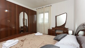 Ein Hotelzimmer mit einem großen Bett, einem hölzernen Kleiderschrank, einem Schminktisch mit Spiegel und einem Fenster mit Vorhängen.