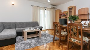 Ein modernes Wohnzimmer mit grauem Sofa, einem Holzespeisetisch, Stühlen, einem kleinen Couchtisch und einem flauschigen, grauen Teppich.