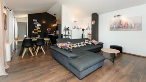 Un salon moderne avec un canapé d’angle gris, une table à manger avec des chaises et une petite table ronde.