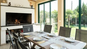 Un coin repas agrémenté d’une cheminée, de grandes fenêtres et d’une vue sur le jardin.
