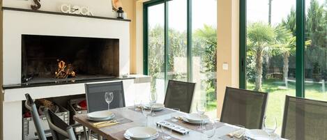 A dining area with a fireplace, large windows, and a view of the garden.