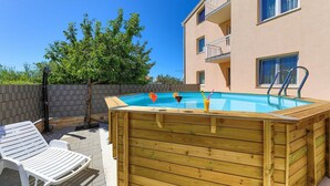 A wooden hot tub with a pool, surrounded by a deck with lounge chairs, a wooden fence, and a building with balconies. - Two Bedroom Apartment with Balcony (Kastel Novi)