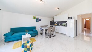 A modern apartment with a teal sofa, a dining area, a kitchen with white cabinets, and a small living room. - Two Bedroom Apartment with Balcony (Kastel Novi)