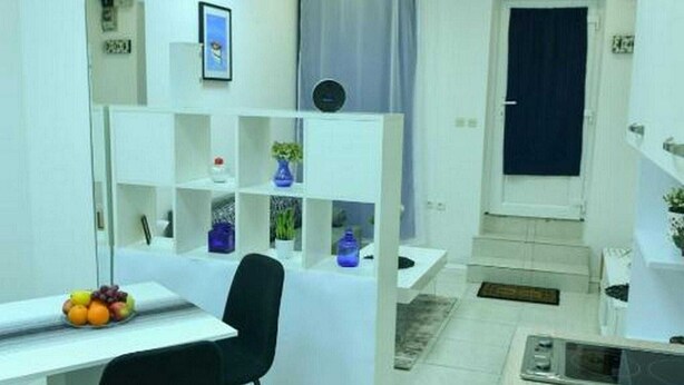 Een moderne, goed verlichte kamer met een wit bureau, zwarte stoelen en een blauwe vaas op een witte plank.