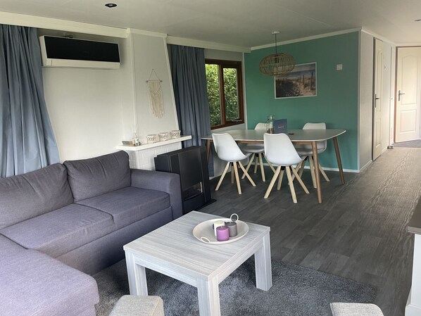 Una sala de estar moderna con un sofá gris, una mesita blanca con una vela y una zona de comedor con una mesa y sillas.