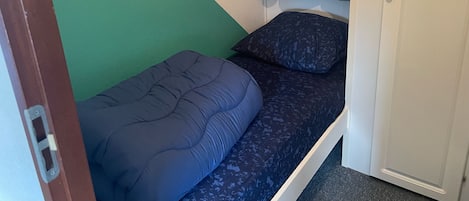A small, narrow room with a bed against the wall, a door on one side, and a green and white wall.