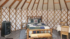 A cozy yurt bedroom with a bed, wooden furniture, a heater, and a table. - Premium Comfort in the Wilderness (Nabesna)