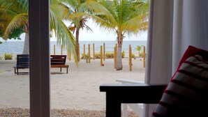 Blick auf einen Strand von einem Zimmer aus, mit einer Bank und Ausblick auf das Meer, Palmen und einem Zaun.