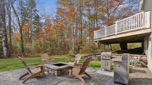 Une terrasse extérieure avec des fauteuils Adirondack, un foyer et un espace barbecue.