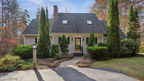 Une maison à deux étages avec un porche à l’avant, une cheminée et une allée menant à l’entrée.