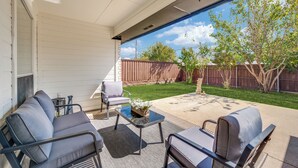 A covered patio with outdoor furniture, a ceiling fan, and a view of a backyard with a wooden fence and trees. - Modern & Spacious 3BD/2BA Luxury in Central Frisco (Frisco)