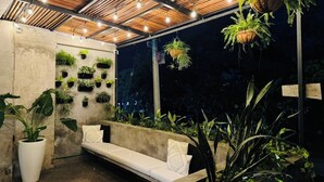 An outdoor seating area with a wooden ceiling, hanging plants, and a concrete wall with potted plants. - Cozy chic studio near the beach! (Puerto Vallarta)
