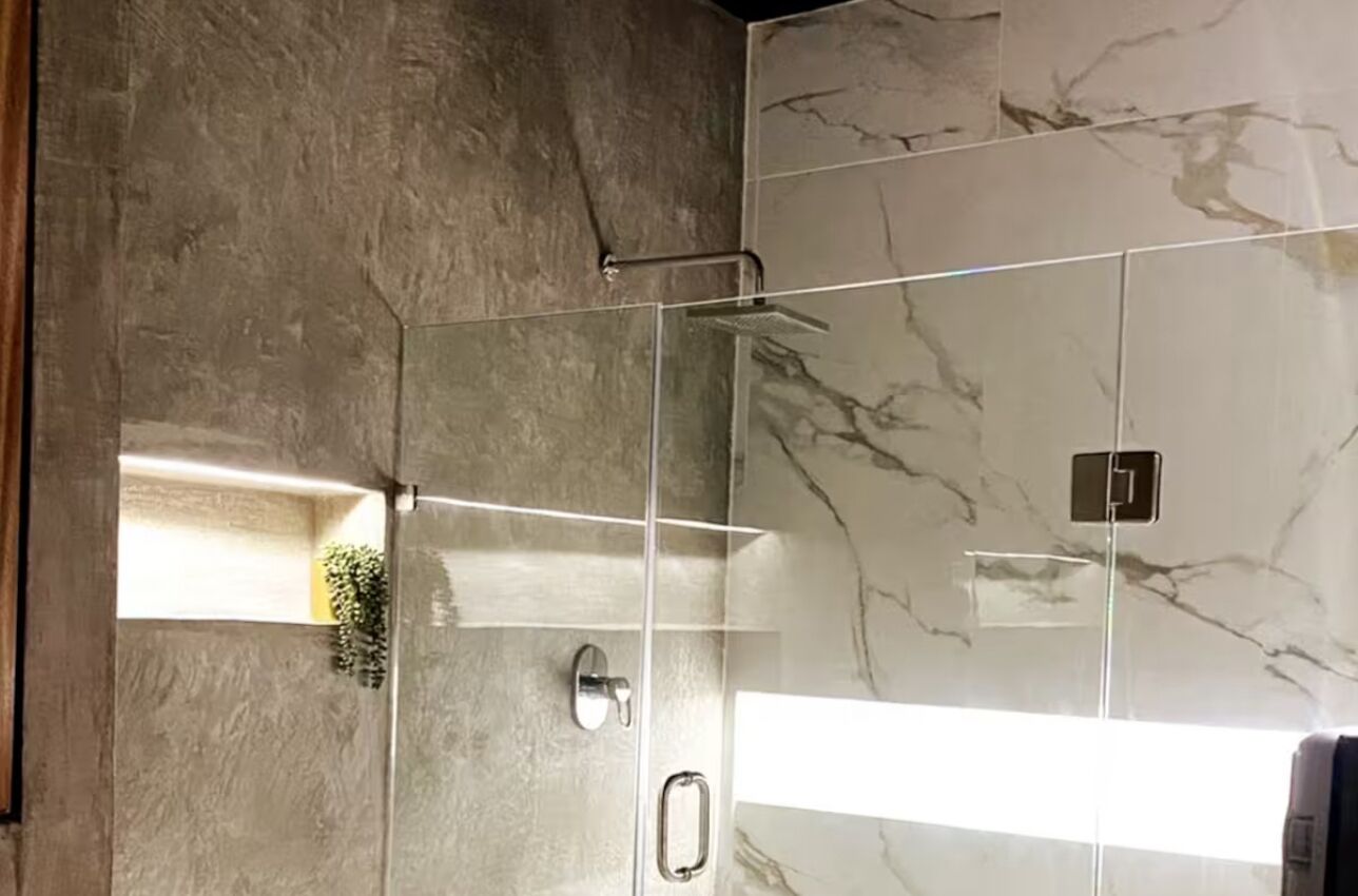 Une salle de bain moderne avec une douche à parois de verre, des murs en marbre et une petite plante sur la gauche.
