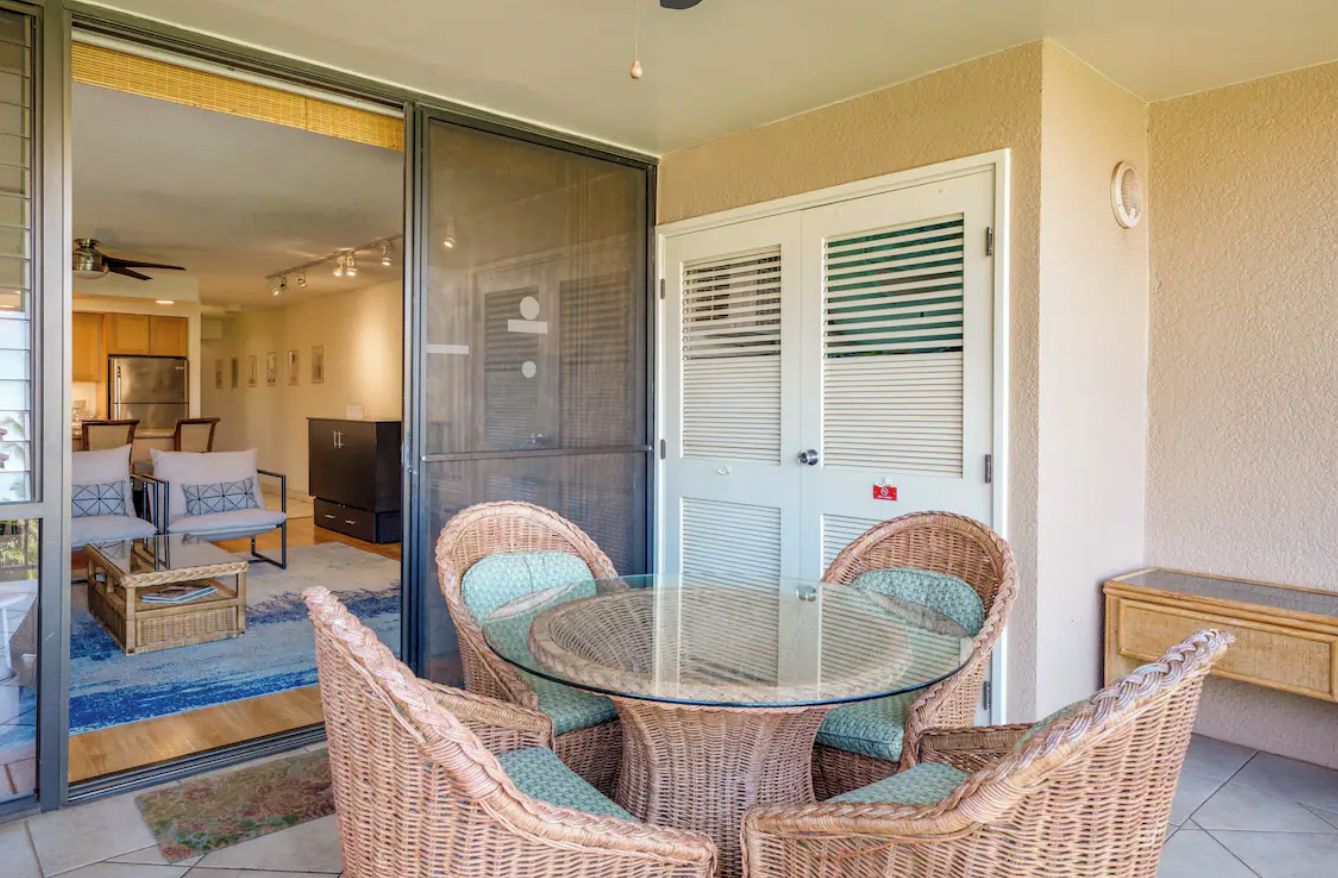 A glass-enclosed patio with wicker furniture, a sliding glass door, and a view into the interior.