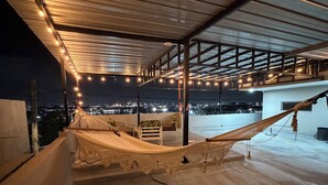 Una terraza en la azotea con una hamaca, vistas panorámicas de la ciudad y luces colgantes.