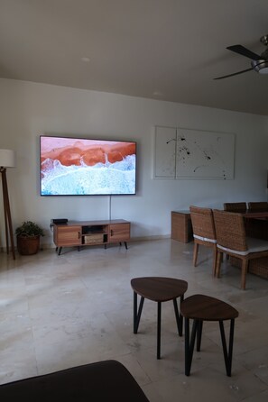 A living room with a flat-screen TV, wooden furniture, and a ceiling fan.