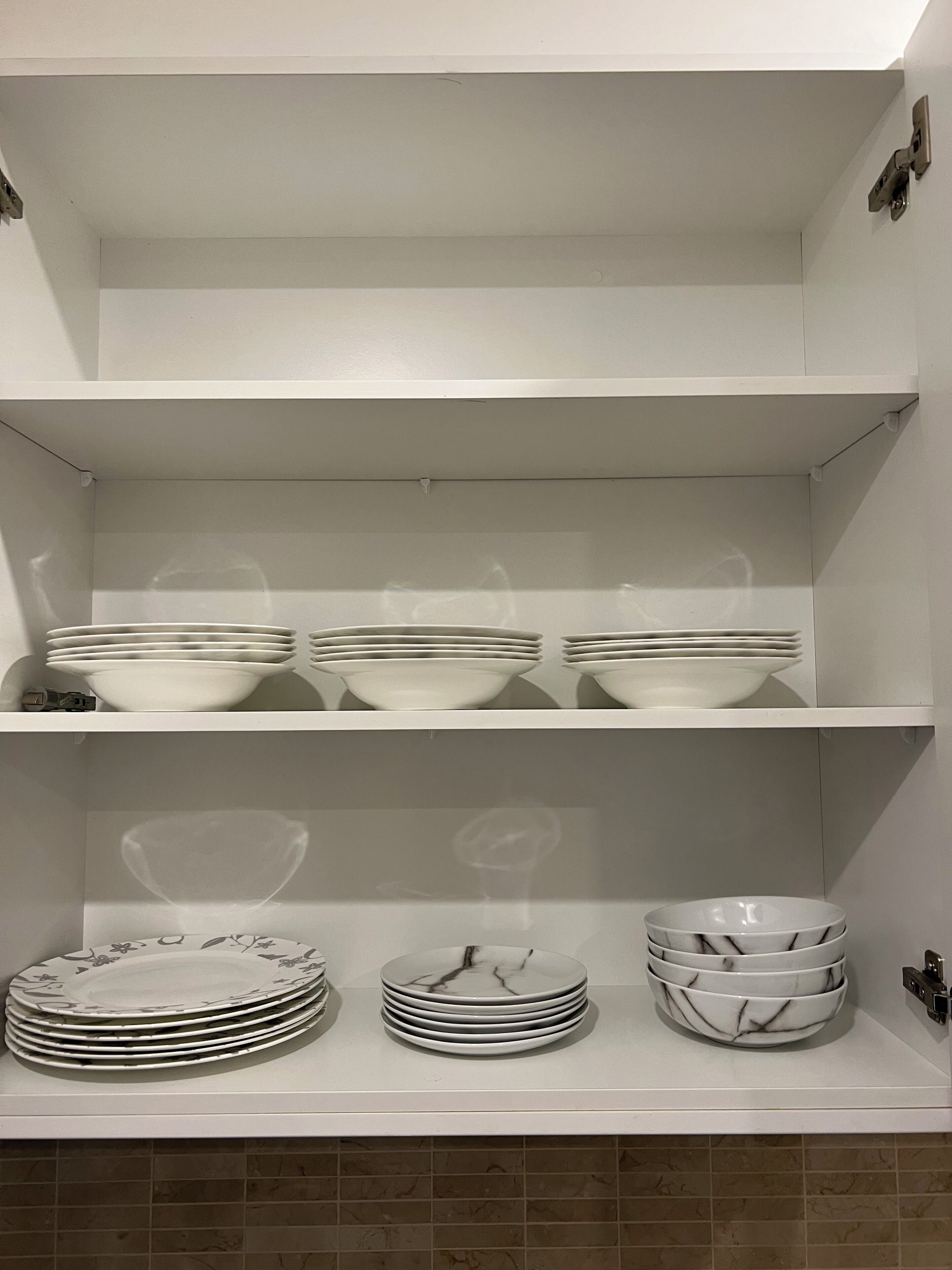 A kitchen with white shelves and tiled backsplash. There are stacks of white plates and bowls on the shelves.