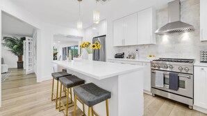 A modern kitchen with white cabinetry, a central island with bar stools, stainless steel appliances, and pendant lighting. - 702A | Waterfront | Sleeps 8 | Heated Pool |Tiki Hut |Fire Pit |by DelrayNightly (Delray Beach)