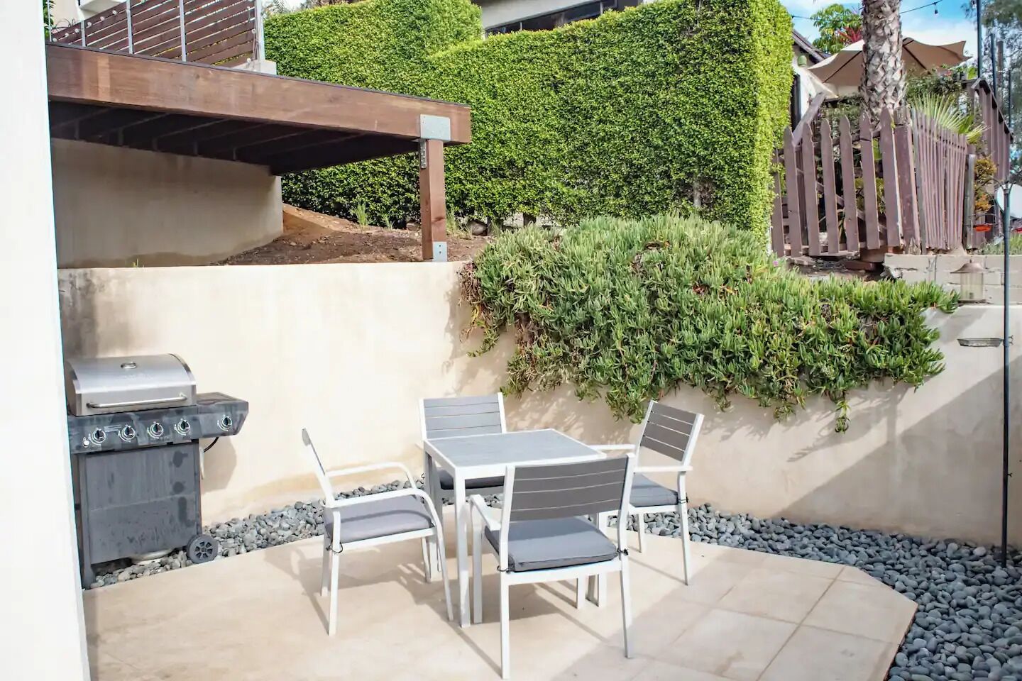 Een terras buiten met een barbecue, tafel en stoelen.