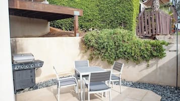 Een terras buiten met een barbecue, tafel en stoelen.