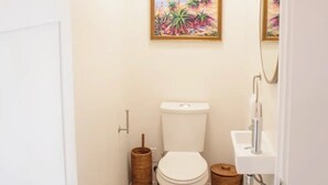Une petite salle de bain propre, équipée de toilettes, d’un lavabo et de deux paniers en bois.
