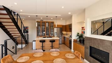 Een moderne keuken met een centraal eiland, ingebouwde apparatuur en een eetgedeelte met een houten tafel en stoelen.