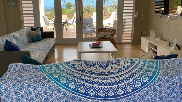 A room with a bed, a table, a sofa, and a balcony with chairs. - Luxurious 6-bedroom villa with Pool, AC, WiFi, panoramic view in charming Rincon (Rincon)