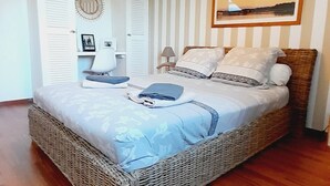 A bedroom with a wicker bed, a bedside table, a lamp, a framed picture on the wall, and a ceiling light fixture.