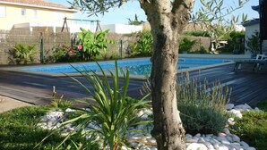 A swimming pool surrounded by a wooden deck, with a tree in the foreground and a fence in the background.