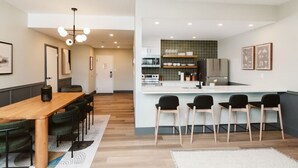A modern kitchen with a central island, wooden dining table, and bar stools.