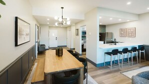 A modern kitchen with a central island, bar stools, and a dining area with a wooden table and chairs.