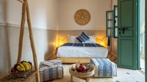 Une chambre à coucher avec un lit, des lampes de chevet, une balançoire en bois, un panier de fruits et une porte verte.