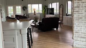 A spacious living area with a high ceiling, wooden beams, a large window, a television, and a fireplace. - 2 Acre  Retreat, Sauna, Fire pit, Decks, Views, 35 Min to Zion, 45 GC, 45-Bryce (Kanab)