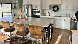 A modern kitchen with white cabinets, a large island with bar stools, stainless steel appliances, and a view of the outdoors. - 2 Acre  Retreat, Sauna, Fire pit, Decks, Views, 35 Min to Zion, 45 GC, 45-Bryce (Kanab)