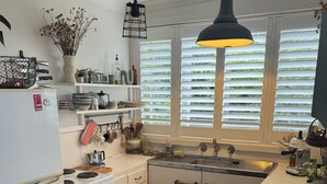 Ett kök med vita skåp, en spis, en ugn och ett fönster med persienner.