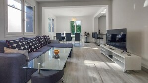 Een moderne woonkamer met een bank, salontafel, televisie en een eethoek met stoelen en een tafel.