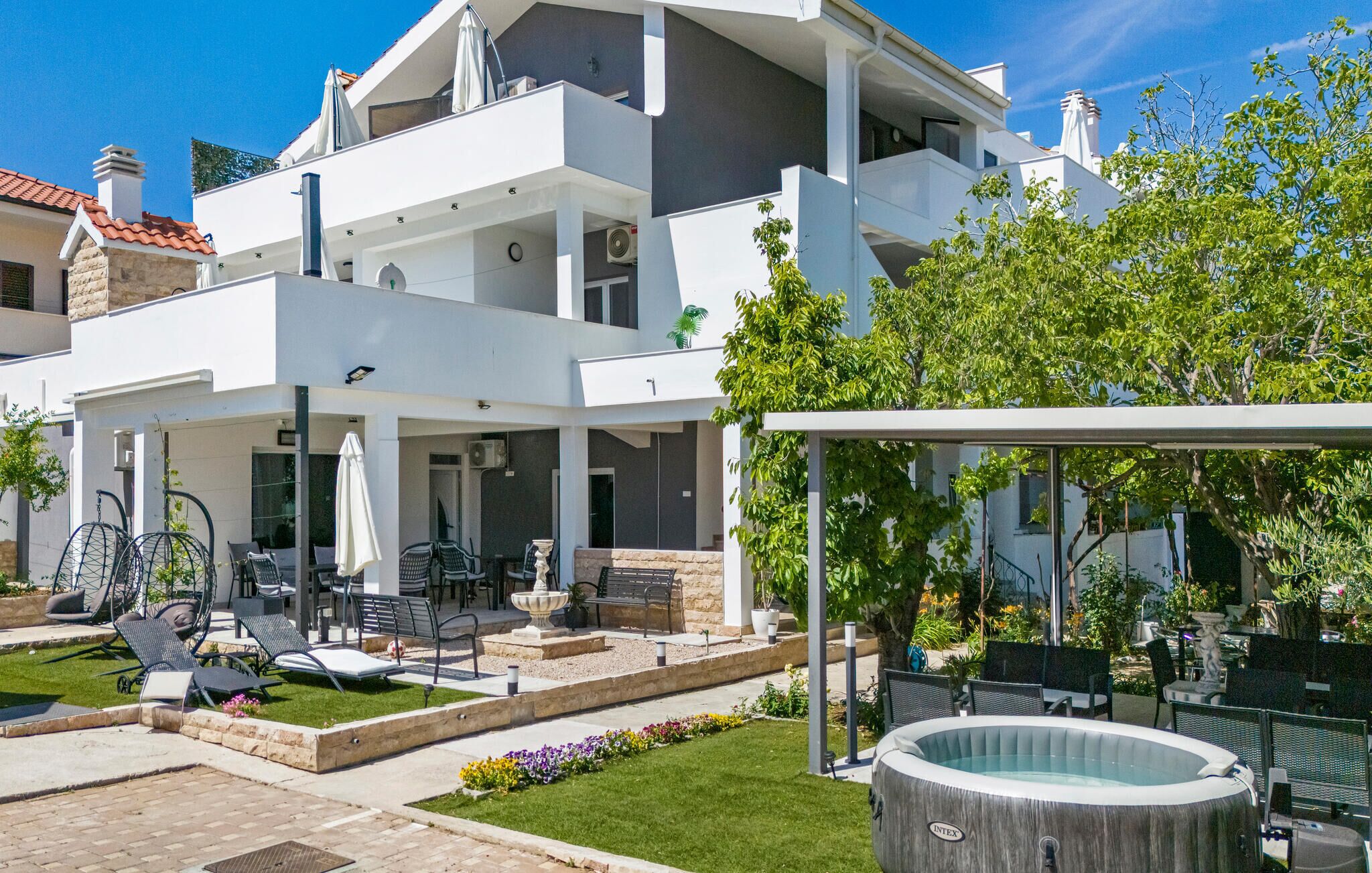 Ein modernes, zweistöckiges Haus mit überdachter Terrasse, Gartenmöbeln und einem Swimmingpool.