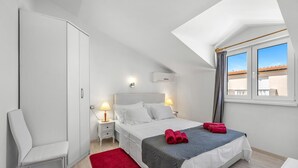 A bedroom with a bed, bedside lamps, a red rug, a window with a view, and a wardrobe. - Luxurious apartment in Vodice with house sea view (Vodice)