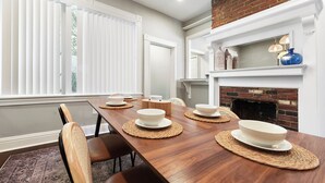 A dining area with a long wooden table, white chairs, and a brick fireplace. - *Regal Bricks* Oversized Deck | Views | Fire Pit | Private Garage (Pittsburgh)