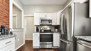 A modern kitchen with stainless steel appliances, white cabinetry, and a wooden floor. - *Regal Bricks* Oversized Deck | Views | Fire Pit | Private Garage (Pittsburgh)