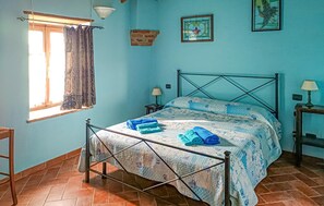 A bedroom with a bed, a window with curtains, a nightstand, a lamp, and a wall with a framed picture. - Awesome apartment in Monticiano (Monticiano)